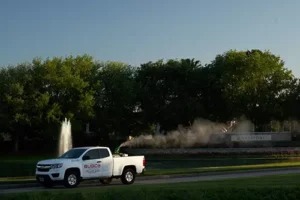 A white truck sprays for mosquitos in a landscaped area.