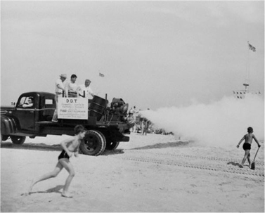Historic black and white photo of a truck spraying DDT on a beach.