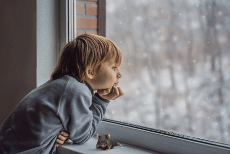 A child gazes out a window at falling snow.
